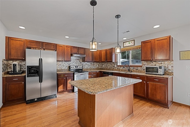 kitchen with pendant lighting, a center island, light stone counters, stainless steel appliances, and light hardwood / wood-style flooring