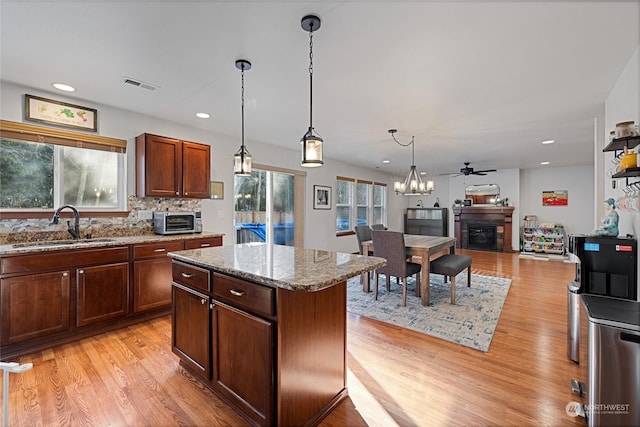 kitchen featuring pendant lighting, sink, a center island, light stone counters, and light hardwood / wood-style floors