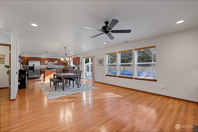 unfurnished dining area with ceiling fan with notable chandelier and light wood-type flooring