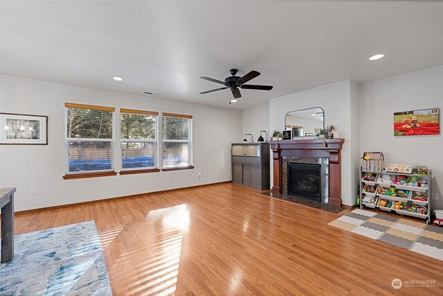 living room featuring a high end fireplace, light hardwood / wood-style floors, and ceiling fan