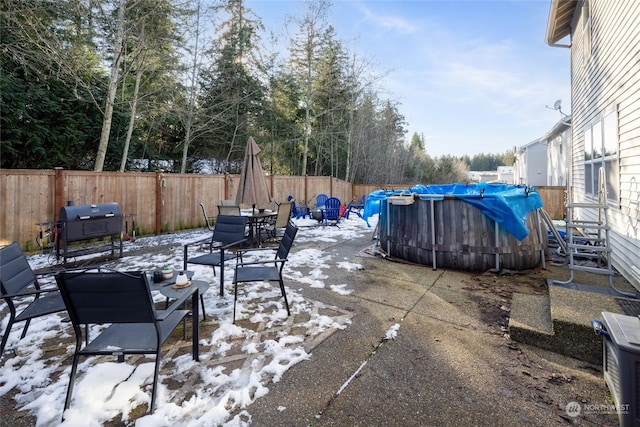 snow covered patio featuring a grill and a fenced in pool