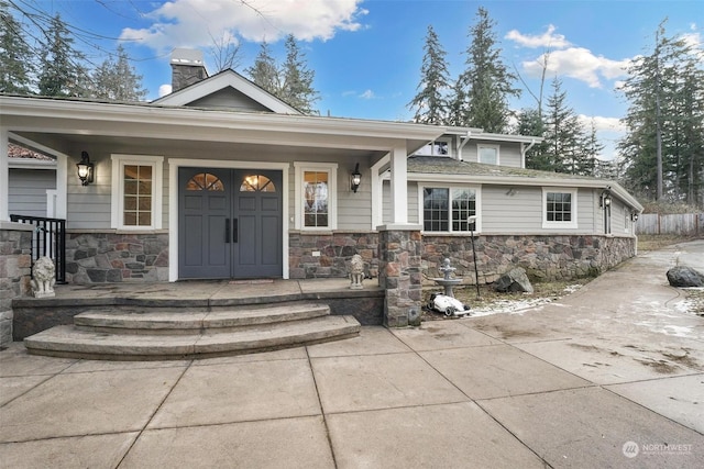 entrance to property with stone siding, covered porch, and a chimney