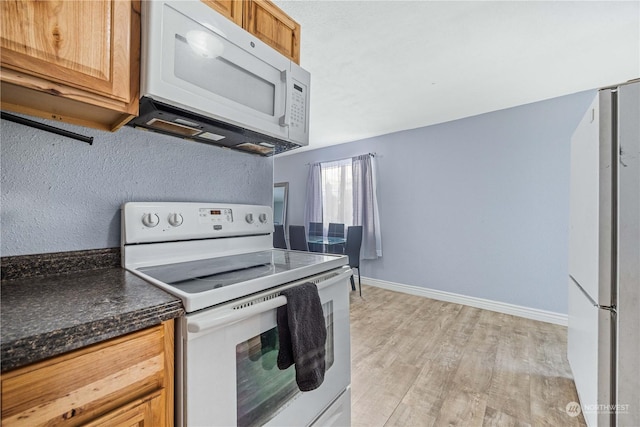 kitchen with dark stone counters, white appliances, and light hardwood / wood-style flooring