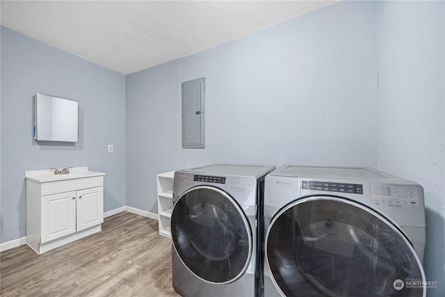 laundry room with electric panel, cabinets, light hardwood / wood-style floors, washer and dryer, and a textured ceiling