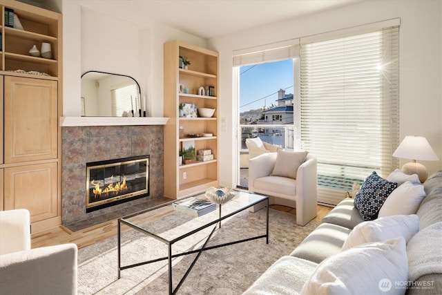 living area featuring built in shelves, wood finished floors, and a tile fireplace