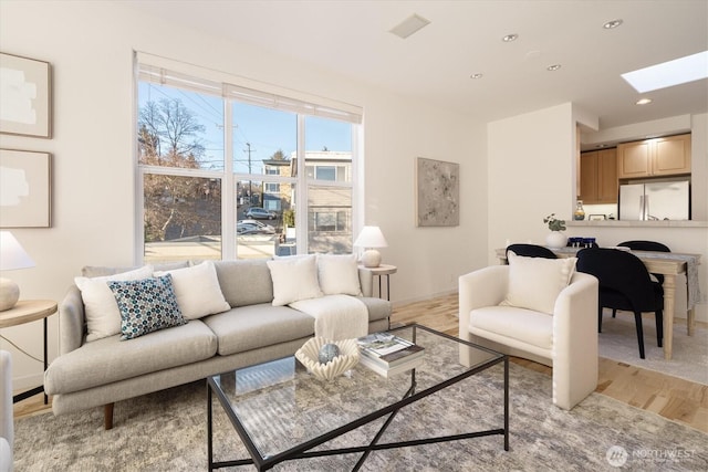 living room with a skylight, recessed lighting, baseboards, and light wood finished floors