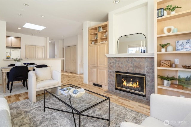 living room with built in shelves, visible vents, a fireplace, recessed lighting, and light wood-style floors