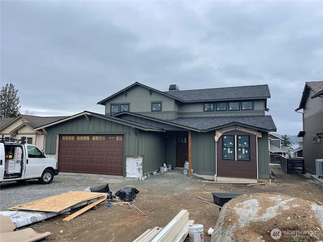 view of front facade with central AC, board and batten siding, an attached garage, a shingled roof, and a chimney