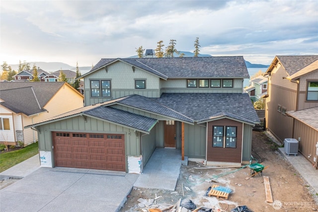 view of front of home with board and batten siding, an attached garage, cooling unit, and roof with shingles