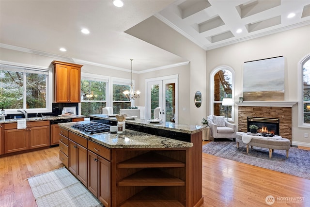 kitchen with a kitchen island, a fireplace, stainless steel gas cooktop, light stone counters, and light wood-type flooring