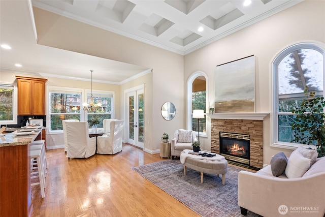 living room with coffered ceiling, an inviting chandelier, light hardwood / wood-style flooring, ornamental molding, and a fireplace