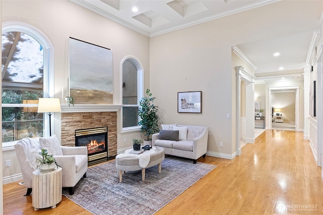 living room featuring crown molding, a stone fireplace, coffered ceiling, and light hardwood / wood-style floors