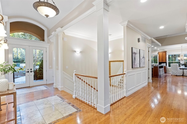 entryway with french doors, ornate columns, a chandelier, ornamental molding, and light hardwood / wood-style floors