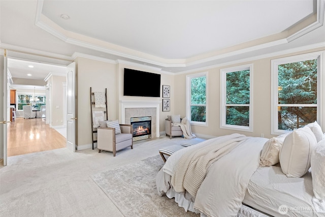 bedroom with a raised ceiling, a tiled fireplace, light colored carpet, and a chandelier