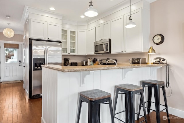 kitchen featuring a breakfast bar, appliances with stainless steel finishes, light stone countertops, white cabinets, and kitchen peninsula