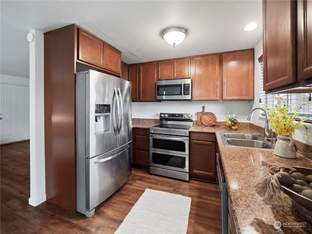 kitchen featuring sink, a textured ceiling, dark hardwood / wood-style flooring, stainless steel appliances, and light stone countertops