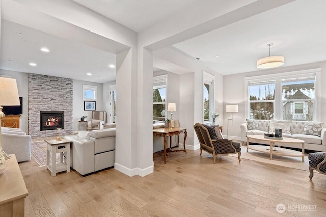 living room featuring light hardwood / wood-style flooring, a wealth of natural light, and a stone fireplace