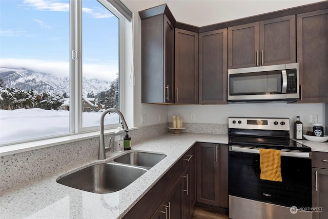 kitchen featuring sink, appliances with stainless steel finishes, dark brown cabinets, light stone counters, and a mountain view