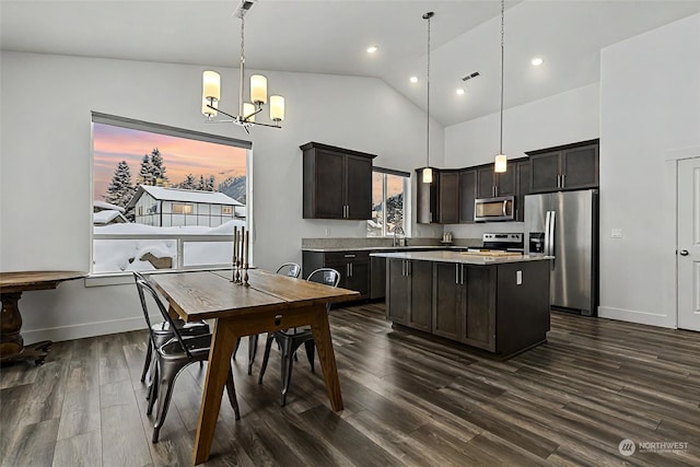 kitchen with dark wood-type flooring, dark brown cabinets, hanging light fixtures, appliances with stainless steel finishes, and a kitchen island