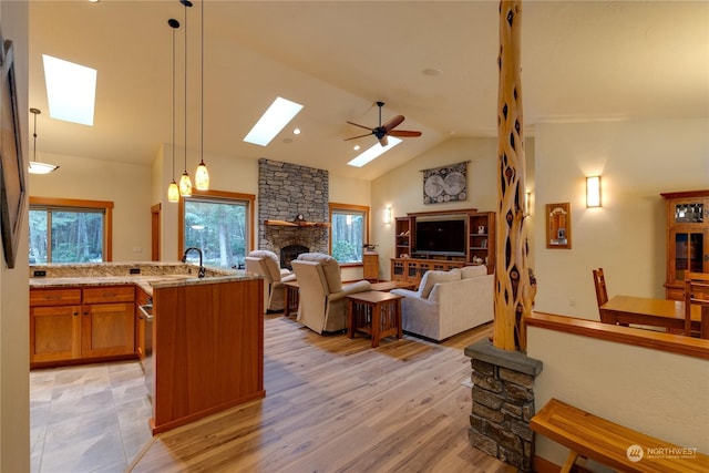 living room featuring ceiling fan, light wood-type flooring, vaulted ceiling with skylight, and a fireplace