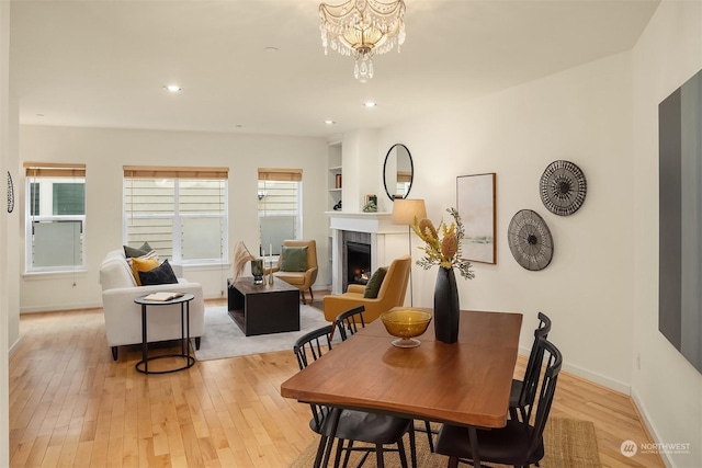 dining space featuring light wood-type flooring, an inviting chandelier, and a fireplace