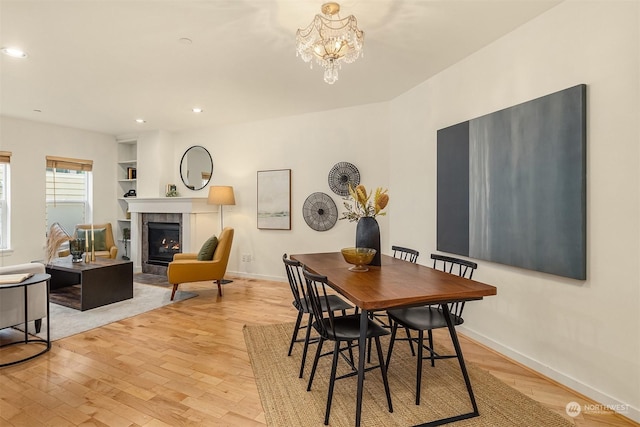 dining room featuring an inviting chandelier, built in features, a fireplace, and light hardwood / wood-style flooring