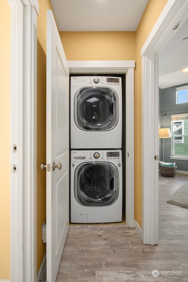 clothes washing area with stacked washer / drying machine and light hardwood / wood-style floors