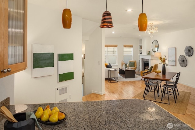 kitchen featuring tile countertops, a lit fireplace, light wood-style floors, and hanging light fixtures