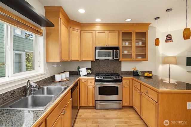 kitchen with a sink, decorative light fixtures, stainless steel appliances, light wood-type flooring, and glass insert cabinets