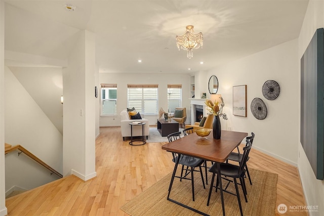 dining room featuring recessed lighting, light wood-style flooring, an inviting chandelier, baseboards, and a warm lit fireplace