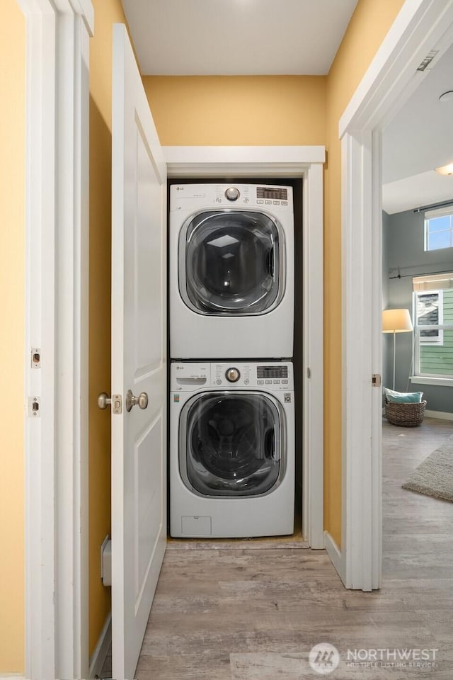 laundry room featuring baseboards, light wood finished floors, stacked washer and dryer, and laundry area