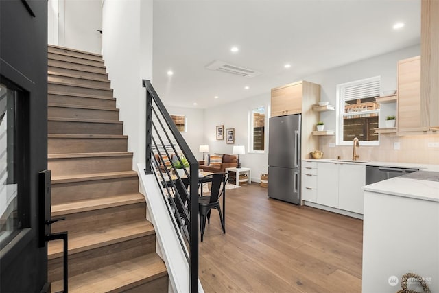 kitchen featuring light brown cabinetry, sink, stainless steel appliances, light hardwood / wood-style floors, and decorative backsplash