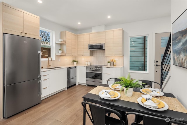 kitchen featuring high end appliances, sink, backsplash, and light wood-type flooring