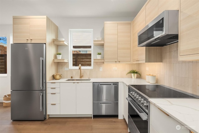 kitchen with sink, backsplash, light stone counters, light hardwood / wood-style floors, and stainless steel appliances