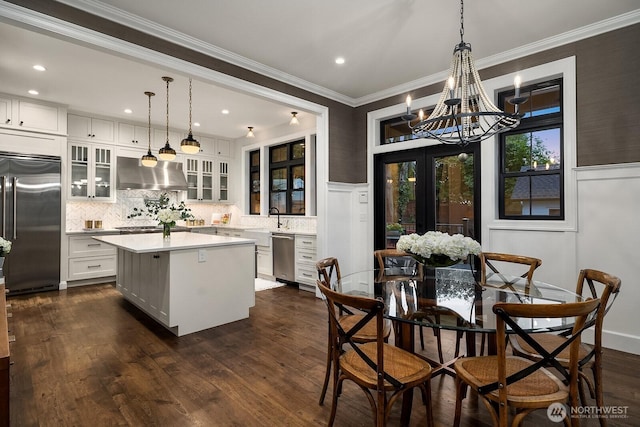 kitchen featuring exhaust hood, light countertops, appliances with stainless steel finishes, a center island, and glass insert cabinets