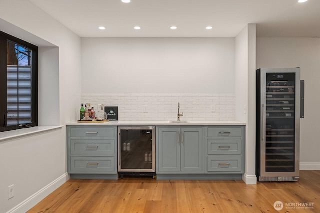 bar featuring light wood-style floors, wine cooler, wet bar, and a sink