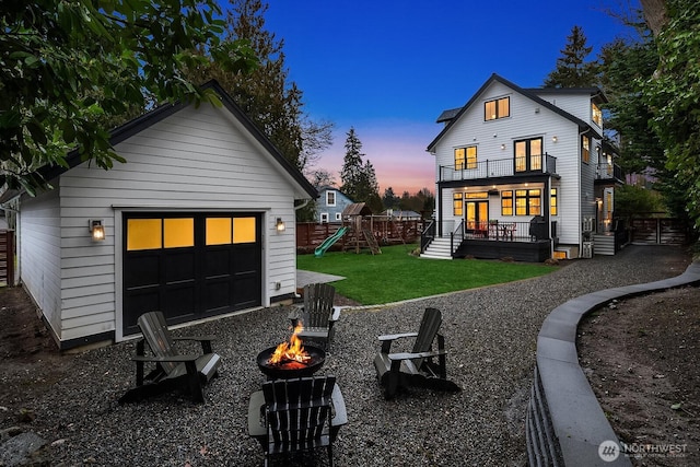 back of house featuring a playground, a balcony, a fire pit, an outdoor structure, and a lawn