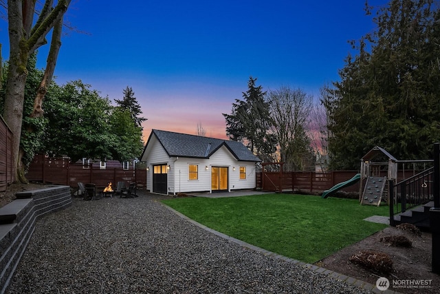 back of house at dusk featuring roof with shingles, a playground, a lawn, a fenced backyard, and an outdoor structure