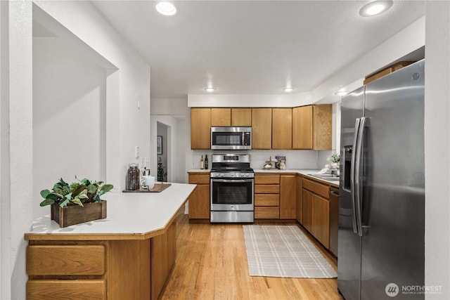 kitchen with a peninsula, light countertops, appliances with stainless steel finishes, light wood-type flooring, and brown cabinetry