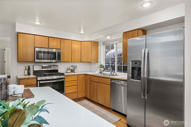 kitchen featuring brown cabinets, light wood finished floors, light countertops, appliances with stainless steel finishes, and a sink