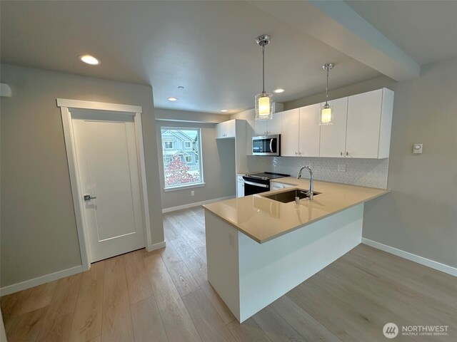 kitchen with stainless steel microwave, light countertops, white cabinetry, pendant lighting, and a sink