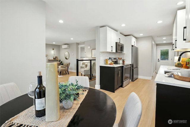 kitchen with sink, white cabinetry, light hardwood / wood-style flooring, stainless steel appliances, and backsplash