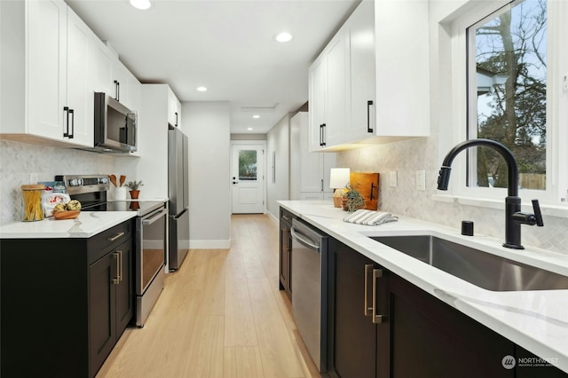 kitchen with stainless steel appliances, sink, a healthy amount of sunlight, light stone countertops, and white cabinets