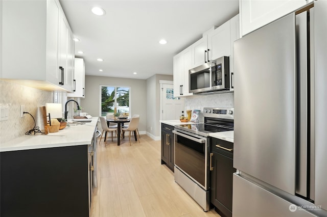 kitchen with appliances with stainless steel finishes, sink, white cabinets, and light hardwood / wood-style flooring