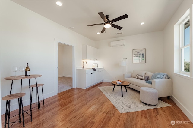 sitting room featuring ceiling fan, a wall mounted AC, sink, and light wood-type flooring