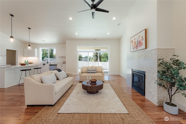 living room with sink, light hardwood / wood-style flooring, ceiling fan, high vaulted ceiling, and a fireplace