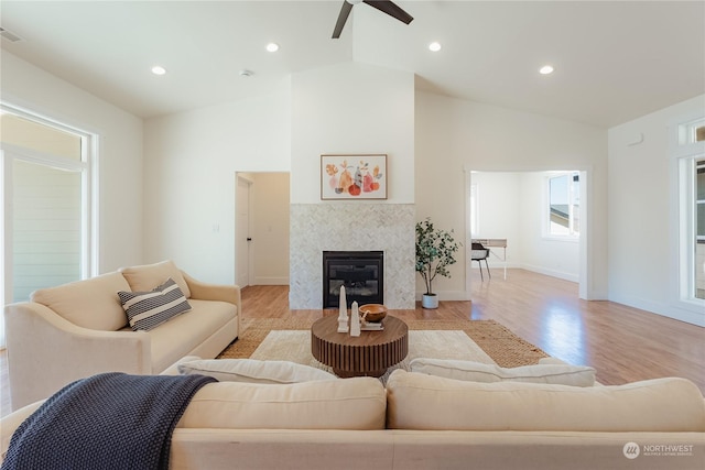 living room with a tile fireplace, high vaulted ceiling, ceiling fan, and light hardwood / wood-style floors