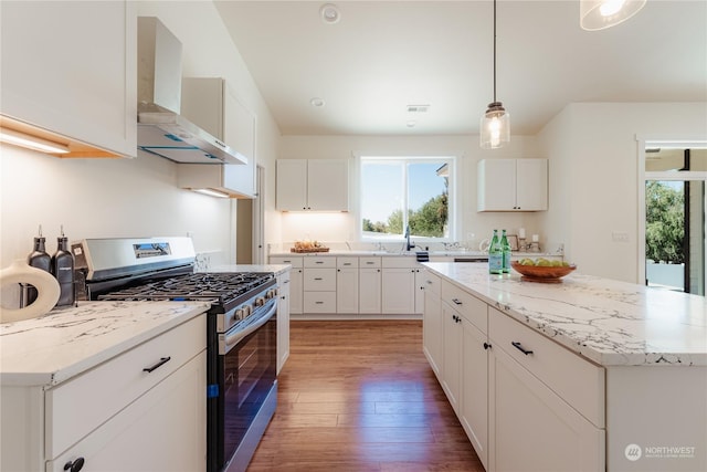 kitchen with a kitchen island, stainless steel range with gas cooktop, decorative light fixtures, white cabinets, and wall chimney exhaust hood