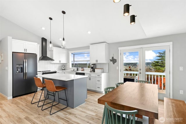 kitchen with white cabinets, wall chimney exhaust hood, light countertops, refrigerator with ice dispenser, and a sink