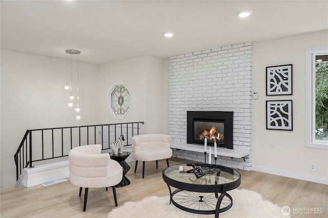 living area featuring recessed lighting, visible vents, light wood-style floors, a brick fireplace, and baseboards